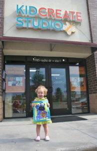 An adorable kid in front of a Kidcreate Studios studio in Ashburn ready to learn more about art history!
